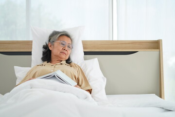Happily elderly woman lying on bed and reading book
