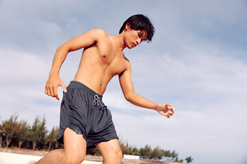 Fototapeta premium Muscular Asian Athlete Running on the Beach, Embracing Fitness and Wellness