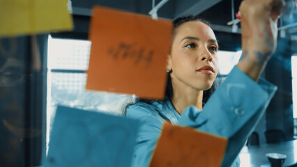 Portrait of smart professional hispanic businesswoman writes marketing ideas on glass board with...