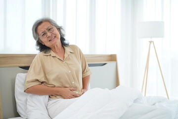 Mature Woman sitting on bed and holding her stomach with feels stomachache