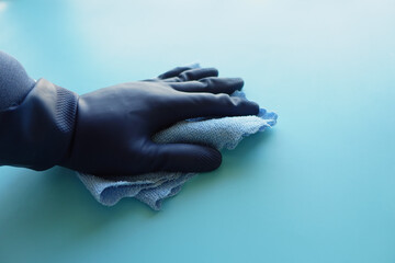 hand in blue rubber gloves cleaning table with cloth 
