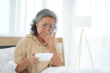 Senior woman wearing glasses sitting on bed hold a bowl with feeling anorexic