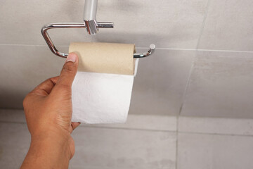 Hand pulling toilet paper roll in holder