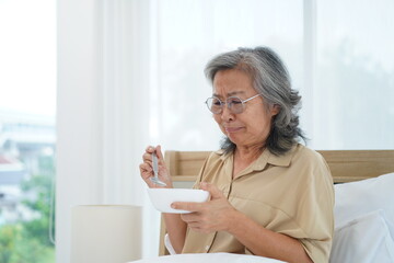 Senior woman wearing glasses sitting on bed hold a bowl with feeling anorexic