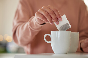 Hand, morning or person with tea bag in home for energy, wellness or break to start day in house kitchen. Begin, prepare or closeup of mug on counter in winter for warm beverage or drink in apartment