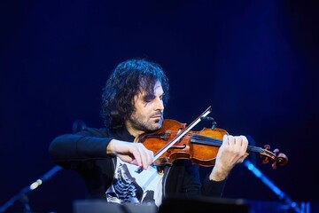A violinist musician stands on stage with a violin in his hands during a concert. There is a bright light from the floodlights around. - 789874621