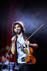 A violinist musician stands on stage with a violin in his hands during a concert. There is a bright light from the floodlights around. - 789874623