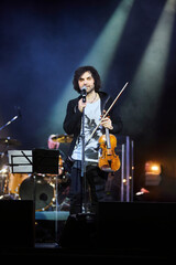 A violinist musician stands on stage with a violin in his hands during a concert. There is a bright...