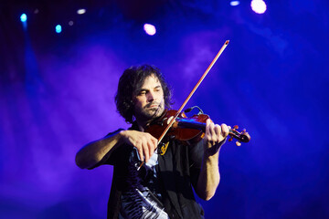 A violinist musician stands on stage with a violin in his hands during a concert. There is a bright light from the floodlights around. - 789874630