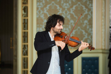Musician violinist with a violin in his hands standing on stage during the concert.