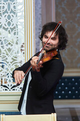 Musician violinist with a violin in his hands standing on stage during the concert. - 789874839