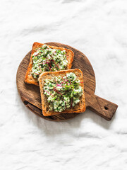 Delicious tapas, appetizer, snack - bruschetta with avocado, eggs, gherkins, greens spread on a wooden chopping board on a light background - 789883668