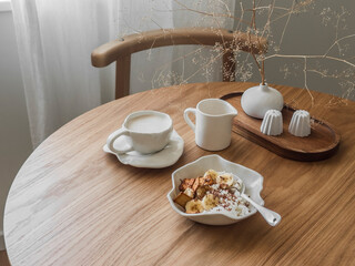 Cozy breakfast, brunch served on a round wooden table - cottage cheese with banana, cookies, chocolate and cappuccino