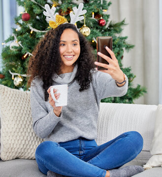 Woman, selfie and Christmas holiday in home with coffee drink as social media post, tree or connection. Female person, cellphone and smile on couch in apartment or festive season, decorations or xmas