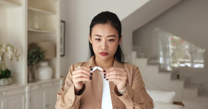 Head shot portrait young serious Asian woman breaks cigarette into two parts. Cessation, quitting smoking decision, breaking free from addiction, personal empowerment, self-control or social awareness