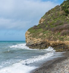 Fototapeta na wymiar not calm Black Sea, beach and steep coast near the green wooded mountains of the Western Caucasus not far from the village of Abrau (South of Russia) on a sunny spring day