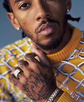 young africane american man posing for a fashion magazine wearing yellow and white patterned sweater, holding his hand on chest with ring finger