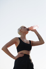 A fit woman in sportswear rests and hydrates with a water bottle after a workout session in an...
