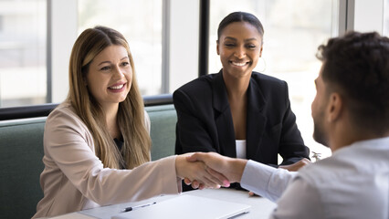 Positive satisfied multiethnic business partners shaking hands at meeting, smiling, ending...