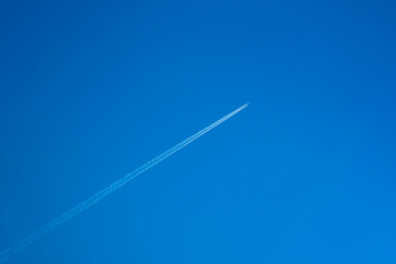 雲ひとつない青空に真っすぐに伸びる飛行機雲 - obrazy, fototapety, plakaty
