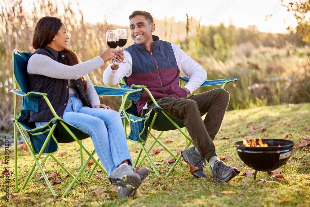 Wall mural Cheers, wine and happy couple camping in park for love, holiday vacation and valentines day picnic. Toast, man and woman with fireplace, smile and chairs on date for anniversary in nature or forest