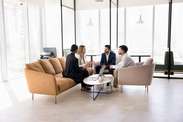 Engaged multiethnic business team sitting in circle on couch, in armchairs in office co-working space, discussing teamwork strategy, solutions for project, talking on collaboration, brainstorming