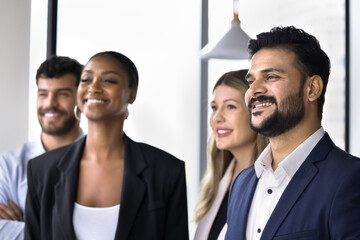 Multiethnic group of young happy business colleagues standing together, promoting successful collaboration, diversity, looking away, smiling. Diverse team and Indian leader man posing for in office