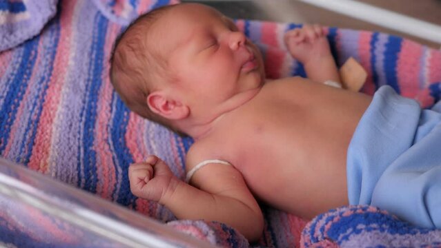 Close-up portrait of a newborn baby in the hospital with tags on the handles in the crib. 