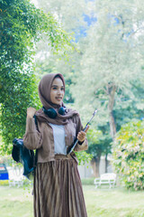 mature asian woman in veil candid smile carrying books and clipboard and bag standing in outdoor park. female students for the themes of education, technology and advertising