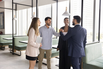 Positive diverse team of managers giving friends handshake, enjoying team success, office friendship, teamwork, synergy, shaking hands with gratitude, approbation