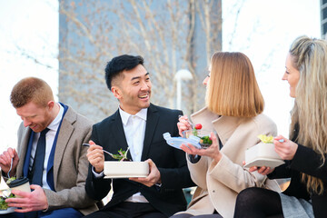Businesspeople on lunch break talking, relaxing and laughing outside office building together.