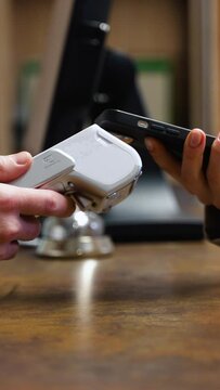 Woman making payment with phone, receptionist holding credit card reader in hotel. Vertical video