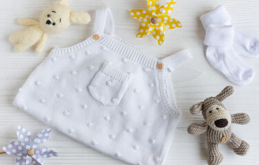 Set of white clothes and accessories for newborn baby. Knitted toys, knitted romper, socks on white wooden background.