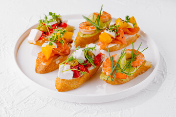 Elegant platter of assorted bruschetta with fresh toppings on a white background