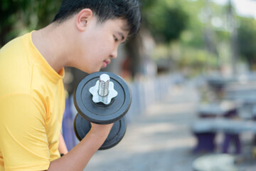 Asian chubby teenboy doing exercise with dumbbells lifting in outdoor park in late afternoon of the day.