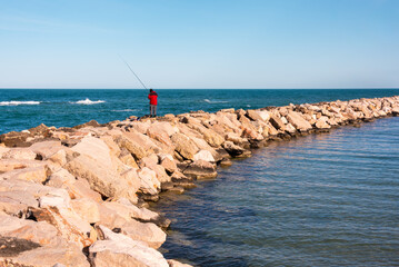Lone fisherman fishing on sea coast - 789939850