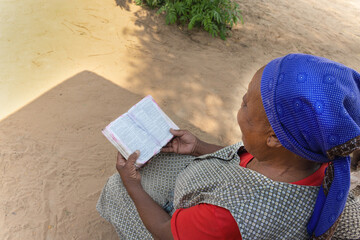 village Christian old african woman ,reading religious holly bible book, casual dressed with blue...