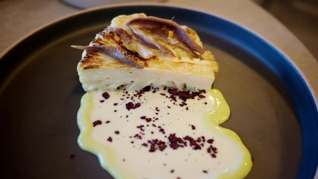 Cauliflower steak with a white sauce on a black plate