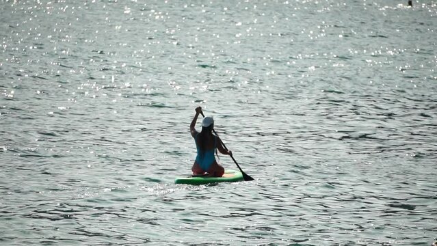Sea woman sup. Silhouette of happy positive young woman in blue bikini, surfing on green SUP board through calm water surface. Idyllic sunset. Active lifestyle at sea or river. Slow motion