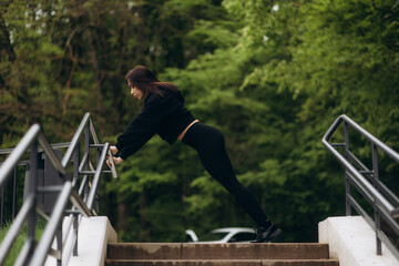 Young attractive woman in sportswear doing a warm-up on stairs before training outdoor in summer day.. Workout, sport, activity, fitness, vacation and training concept.