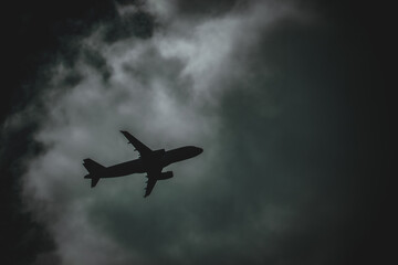 Jet aircraft silhouetted in a night sky flying through a gap in the clouds