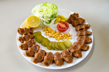 Cig kofte (raw meatball) with lettuce, tomato, pickle and lemon, hot Chee kofta. Turkish local raw food concept.Table scene of assorted take out or delivery foods. Top view of assorted Turkish food.