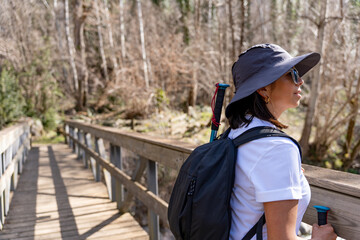 Hiker woman with backpack and hat enjoying the view from a mountain river bridge on a splendid...
