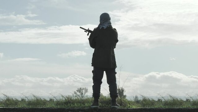 war watchman terrorist standing holding rifle outdoor,rebel soldier separatist guard with gun stands at the vantage point watching out for enemy back view