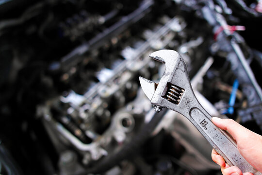 Adjustable wrench or adjustable spanner in a car mechanic hand with car engine blurred background , Car maintenance service concept