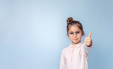 Diligent junior schoolgirl in glasses shares excitement with thumb up gesture. Little girl enjoys school lessons expressing joy with hand gesture