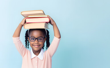 Joyful girl pupil with kinky hair in glasses holds stack of books on head. Little black girl with cheerful smile enjoys funny pastime during school break