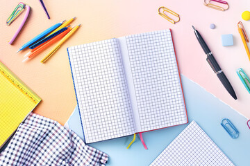 Open notebook with square grid pages lies on study desk among various school stationery. Creative workspace with necessary tools for pupils