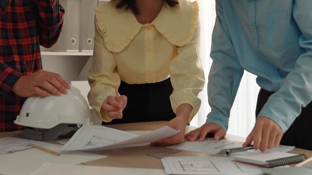 Architect and safety engineer discussion about building blueprint displaying on laptop on table with architectural document and wooden block scatter around at modern office. Closeup. Delineation.