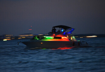 Motorówka podświetlona kolorowymi lampkami płynąca na morzu karaibskim po zachodzie słońca - obrazy, fototapety, plakaty